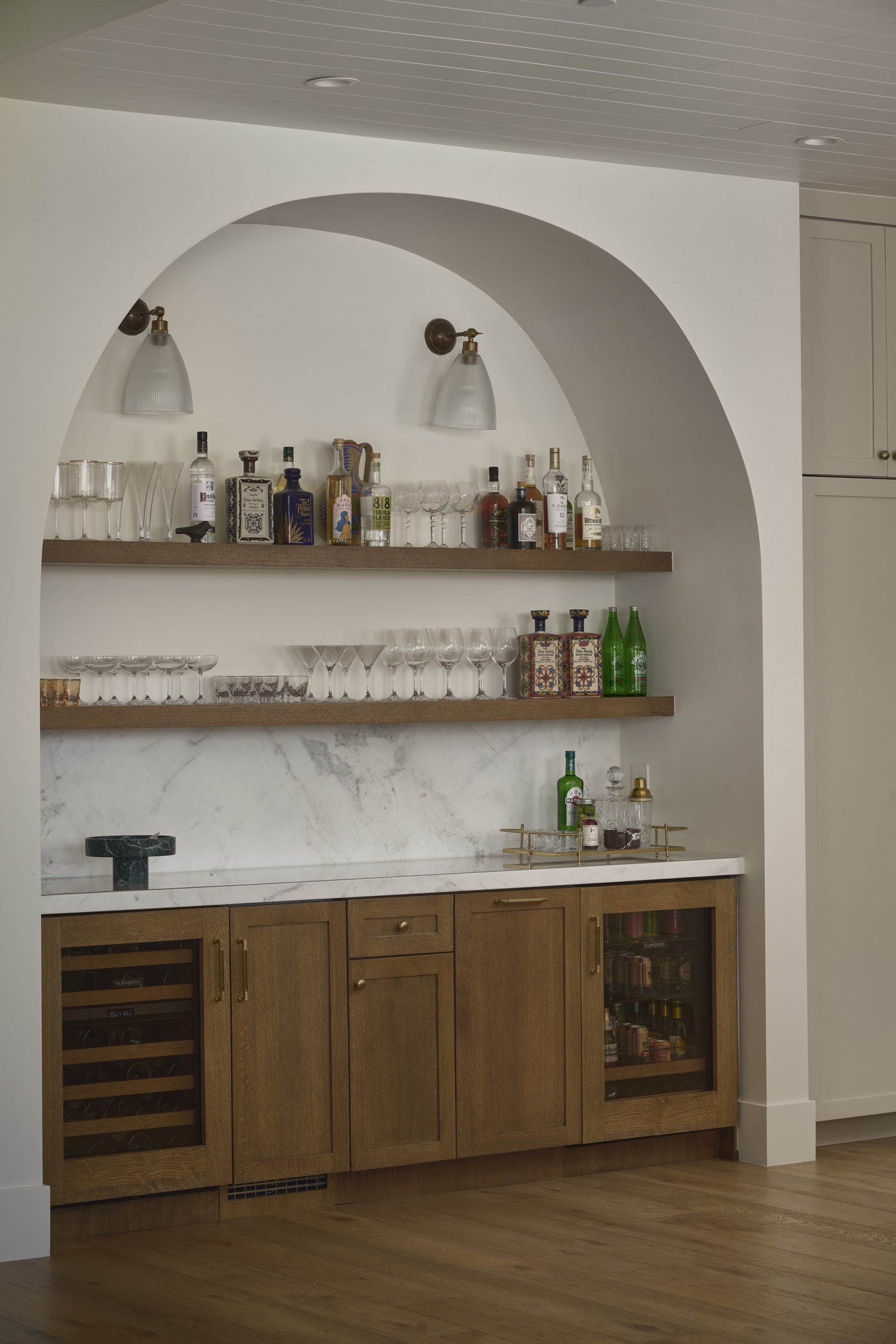 Arched wet bar with wood cabinetry, floating shelves and under-counter beverage refrigerators